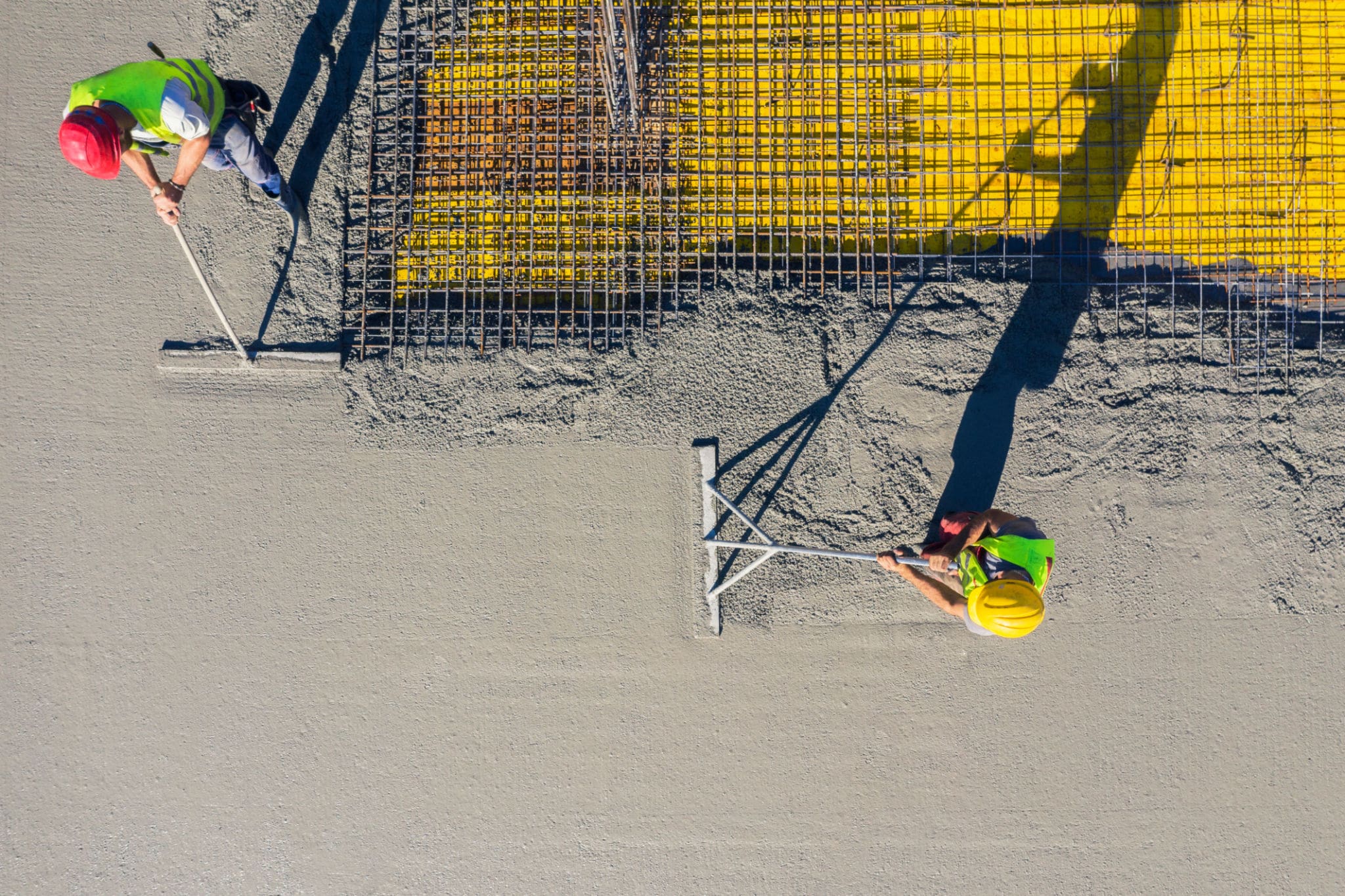 Construction workers leveling wet concrete surface.